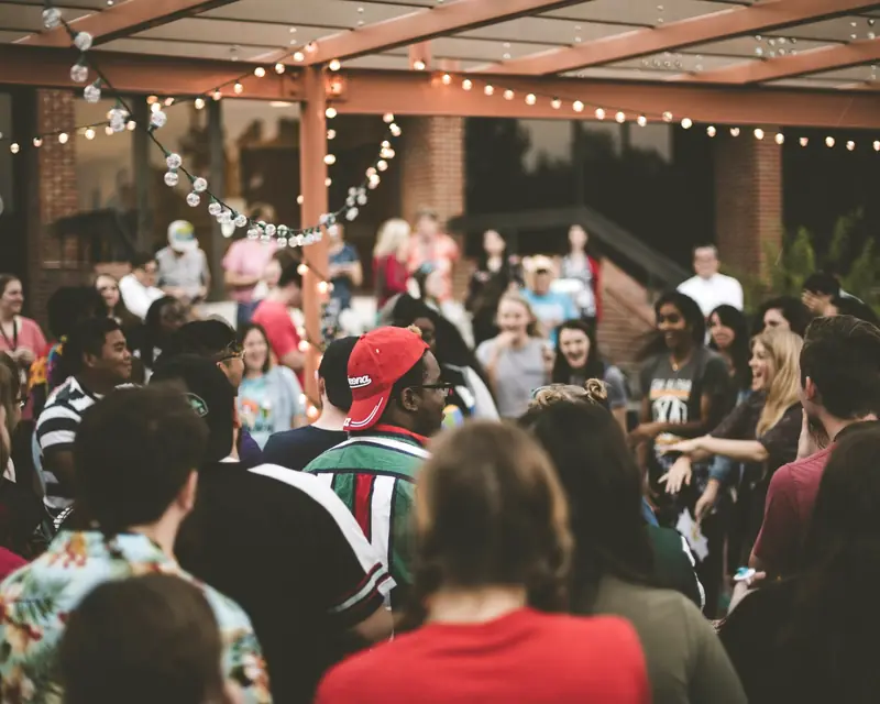 A lively evening crowd gathered under strings of lights on a covered patio