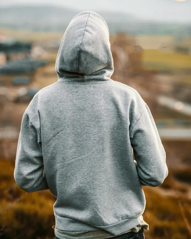 A man in a heavyweight grey hoodie seen from behind, looking out over a valley